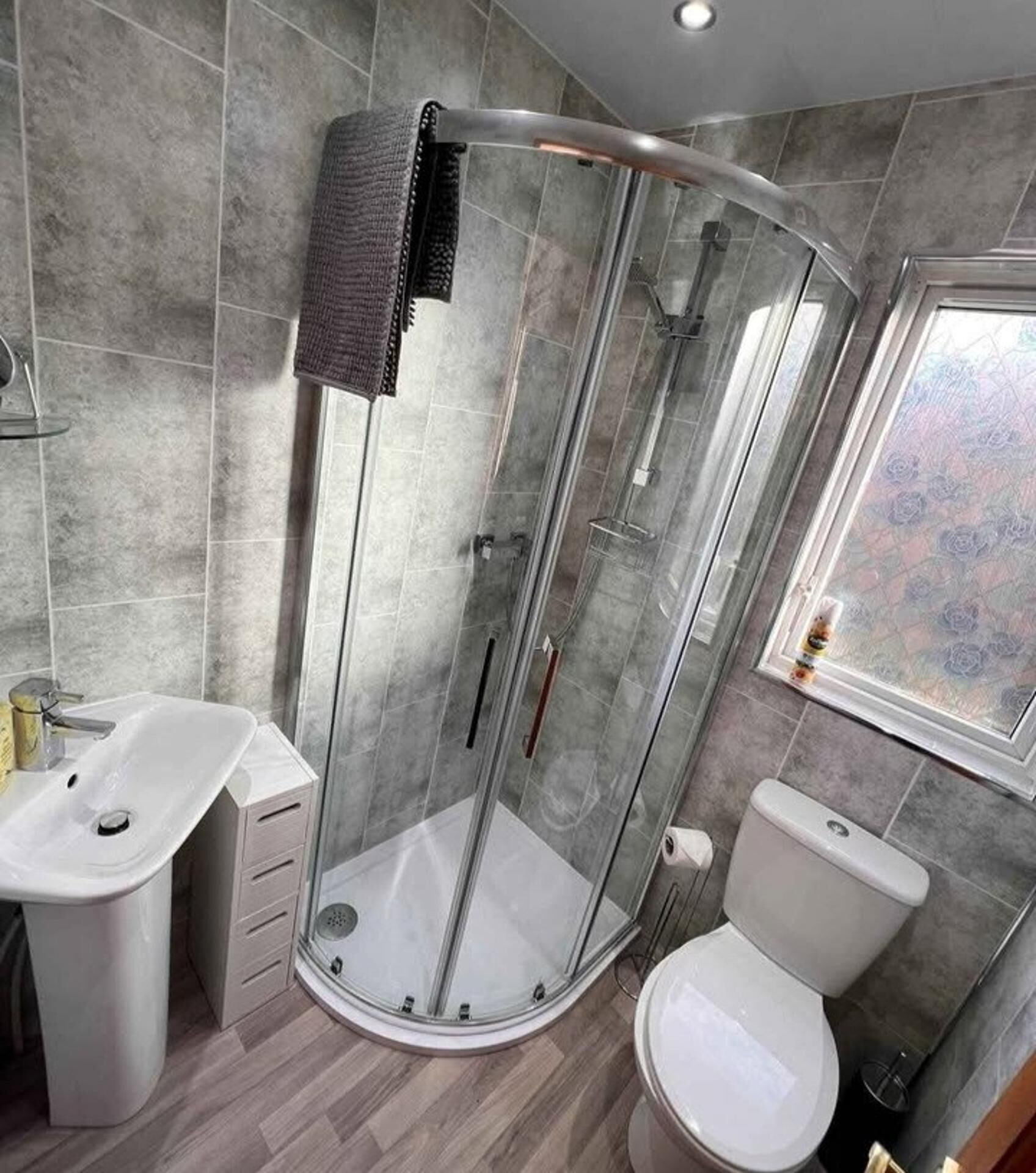 Un baño moderno con ducha de vidrio, un lavabo blanco y un inodoro.