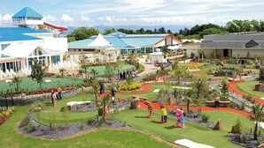 A golf course with a water slide, a small building with a blue roof, and a large white building with a red roof. - Lodge - Sleeps up to 6, pet Friendly & bbq Allowed (Pwllheli)