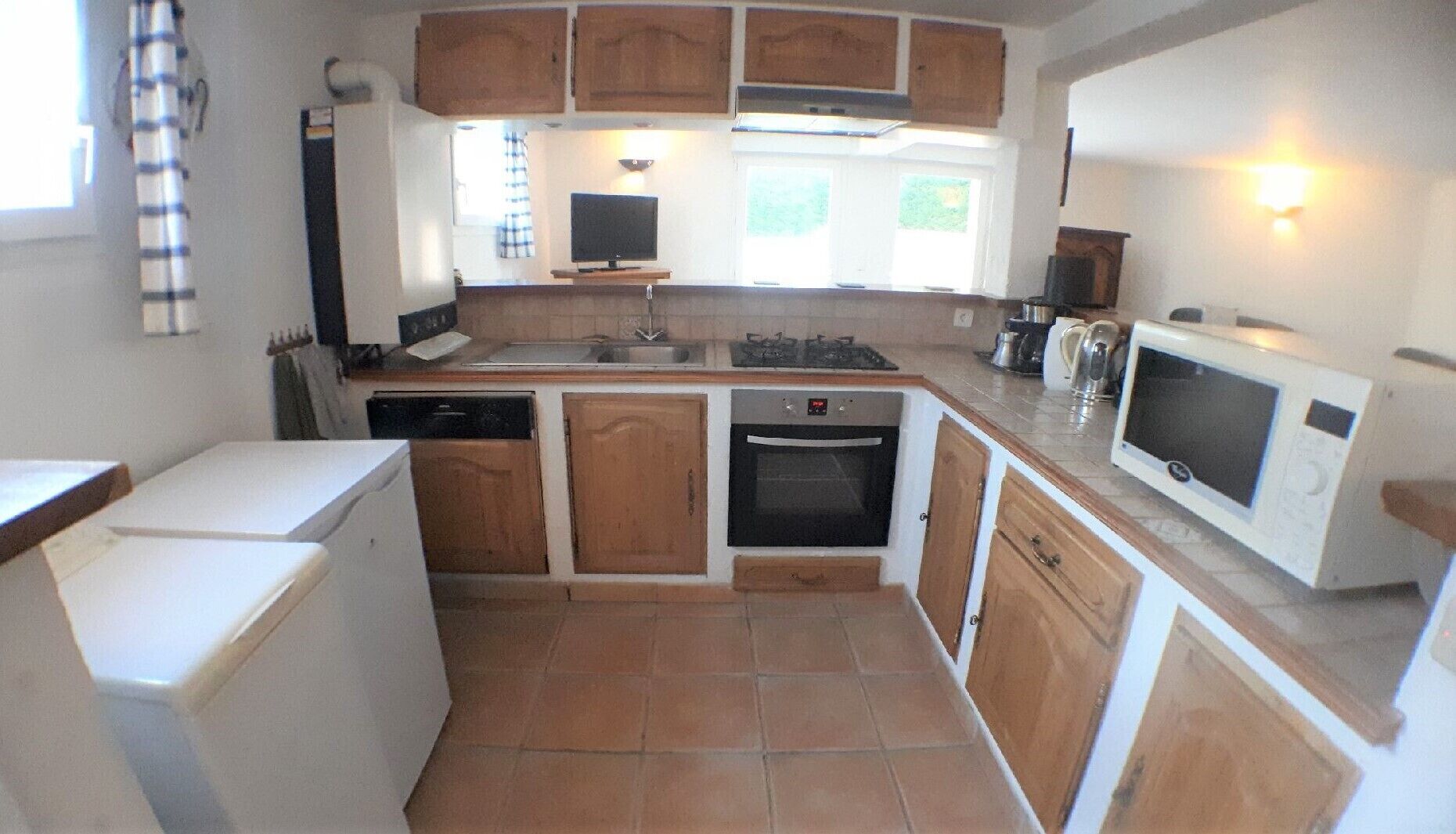 A compact kitchen with wooden cabinets, a dishwasher, an oven, a microwave, and a sink.