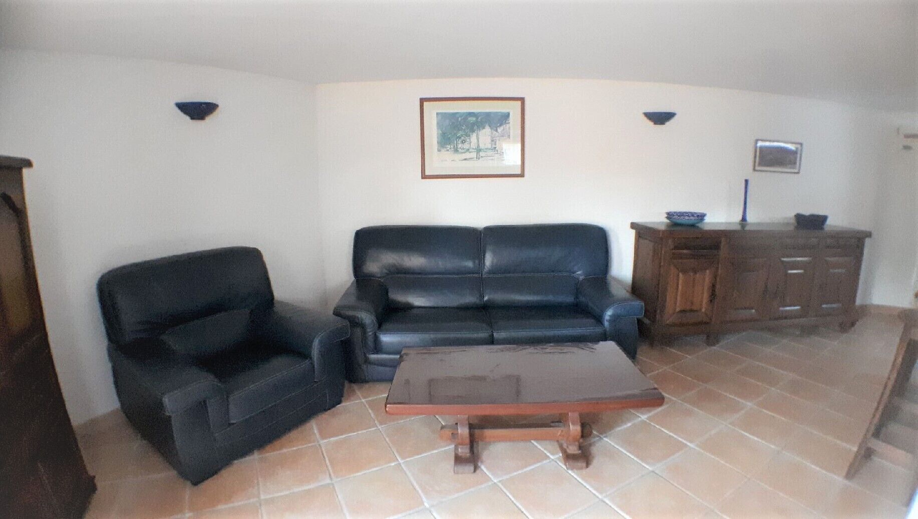 Ein Wohnzimmer mit einer schwarzen Ledersofa, einem Holztisch und einem Schrank.