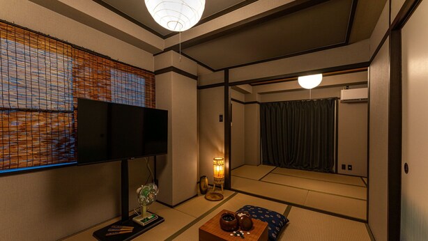 A traditional Japanese room with tatami flooring, a television, a lamp, and a futon bed. - Oyado Kinokuniya Shindaikumachi (Nagasaki)