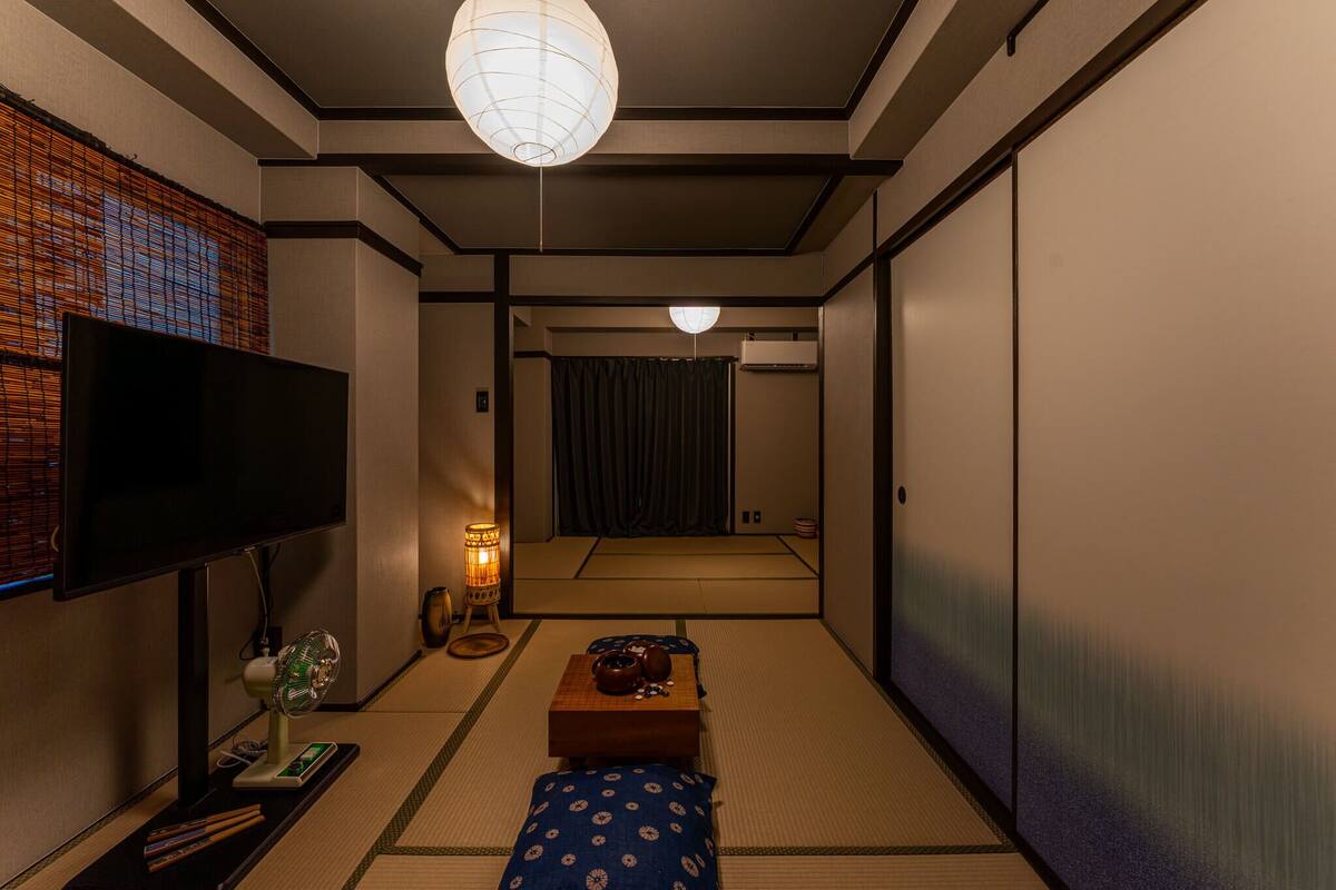 A traditional Japanese room with tatami flooring, a television, a fan, and a sliding door.