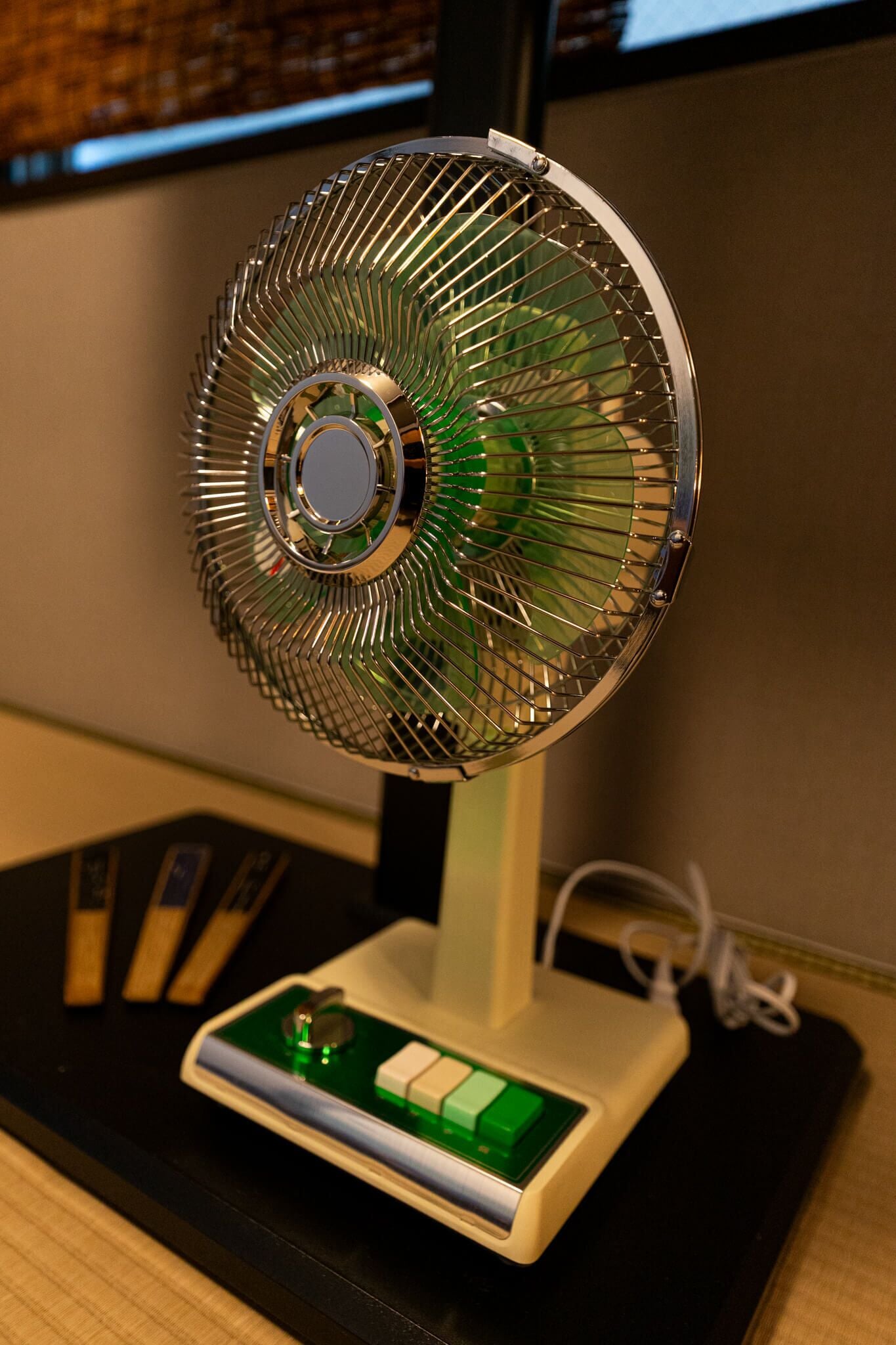 A standing fan with a green and white base, positioned on a black surface.