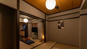 A traditional Japanese room with tatami flooring, a television, a lamp, and a sliding door leading to a kitchen area. - Oyado Kinokuniya Shindaikumachi (Nagasaki)