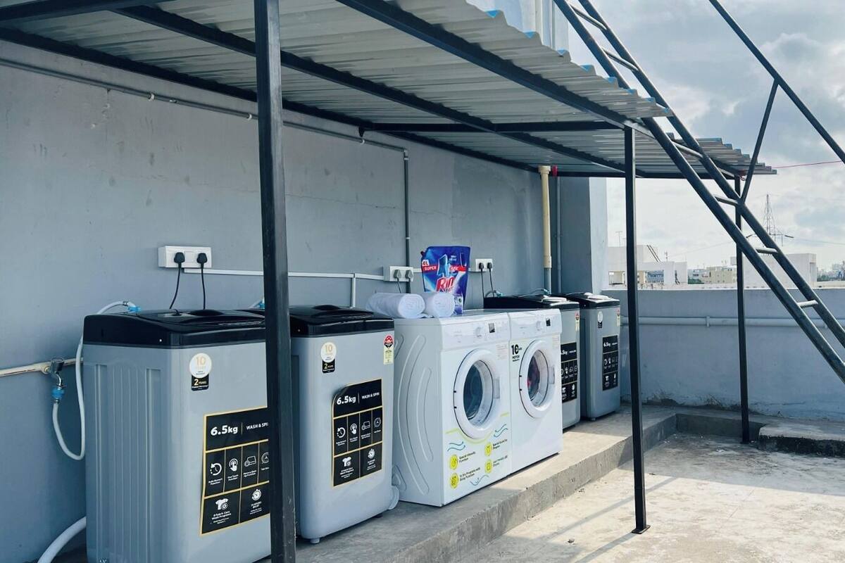 Een wasserette op het dak met drie wasmachines en drogers, een boiler en een metalen trap.