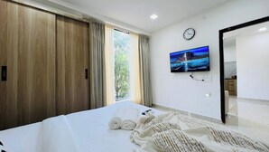 Hotelkamer met een bed, een aan de muur bevestigde televisie, een klok en uitzicht op het omliggende landschap door het raam.