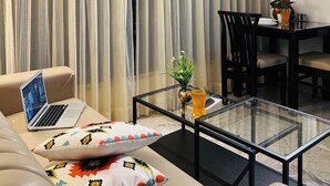 Een moderne woonkamer met een bank, een glazen salontafel, een laptop en een eethoek met een tafel en stoelen.