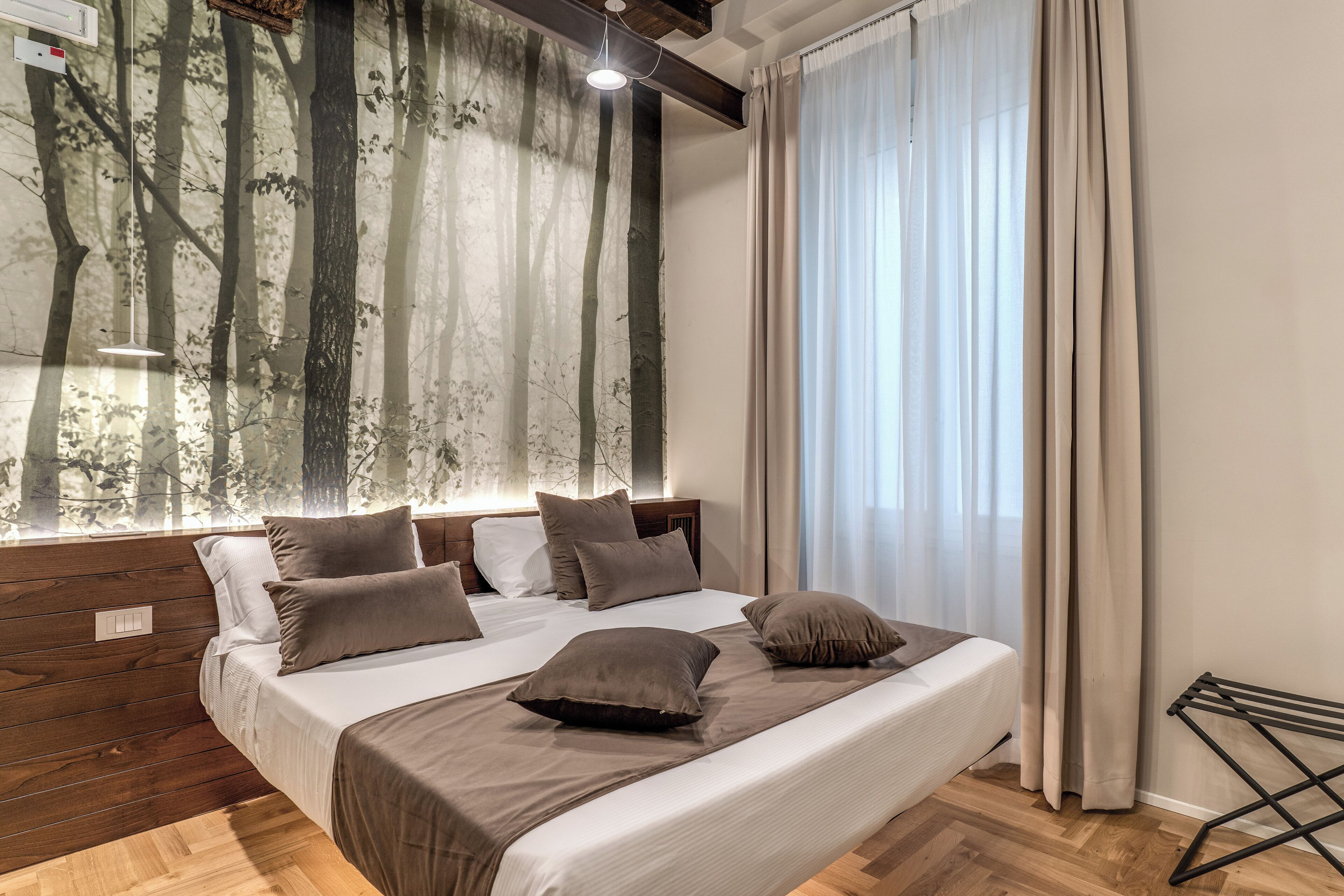 Ein Schlafzimmer mit einem großen Bett, einem Holz-Kopfteil und Blick auf Bäume durch ein Fenster.