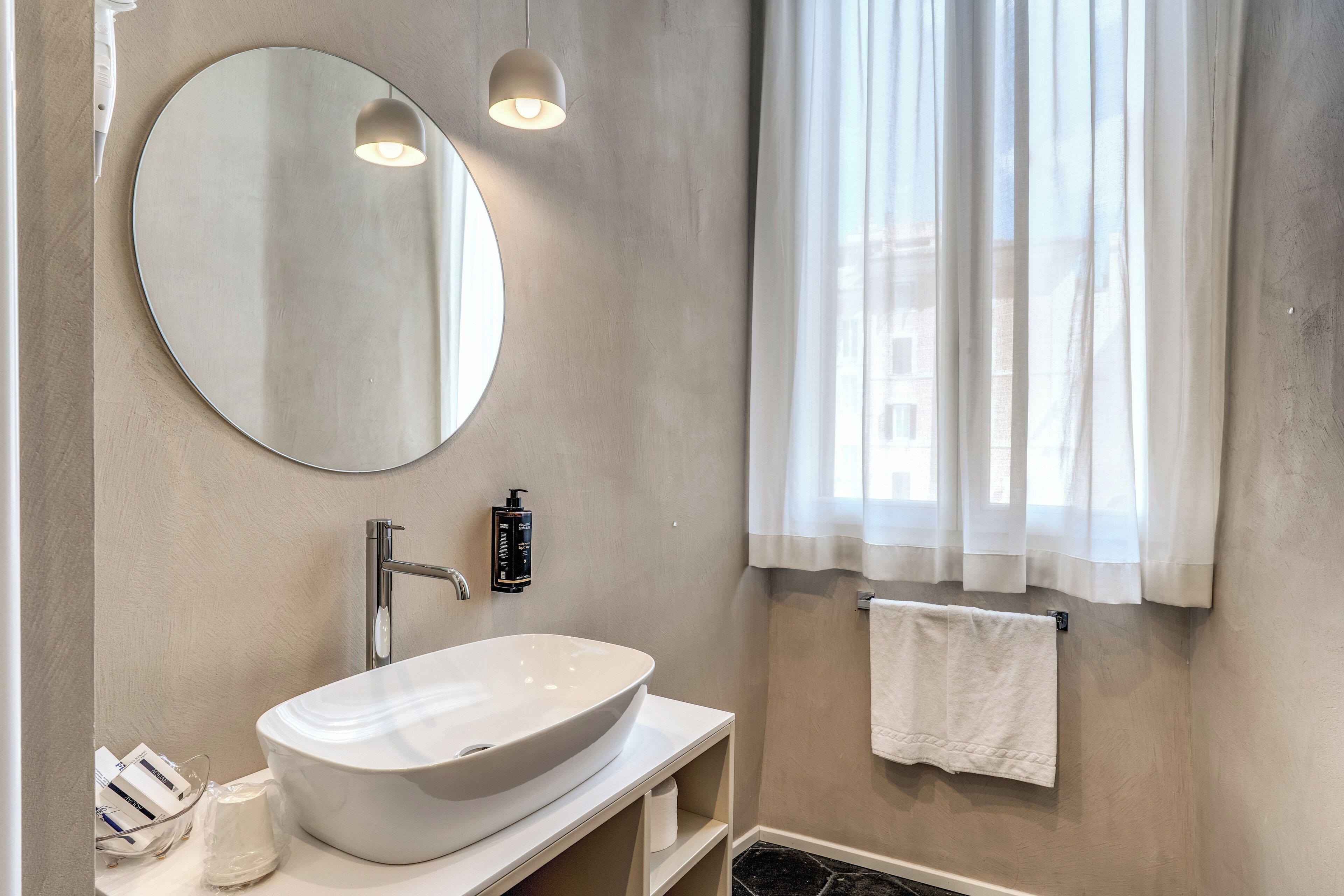 A modern bathroom with a round mirror, a white sink, and a towel hanging on the wall.
