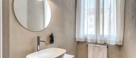 A modern bathroom with a round mirror, a white sink, and a towel hanging on the wall.