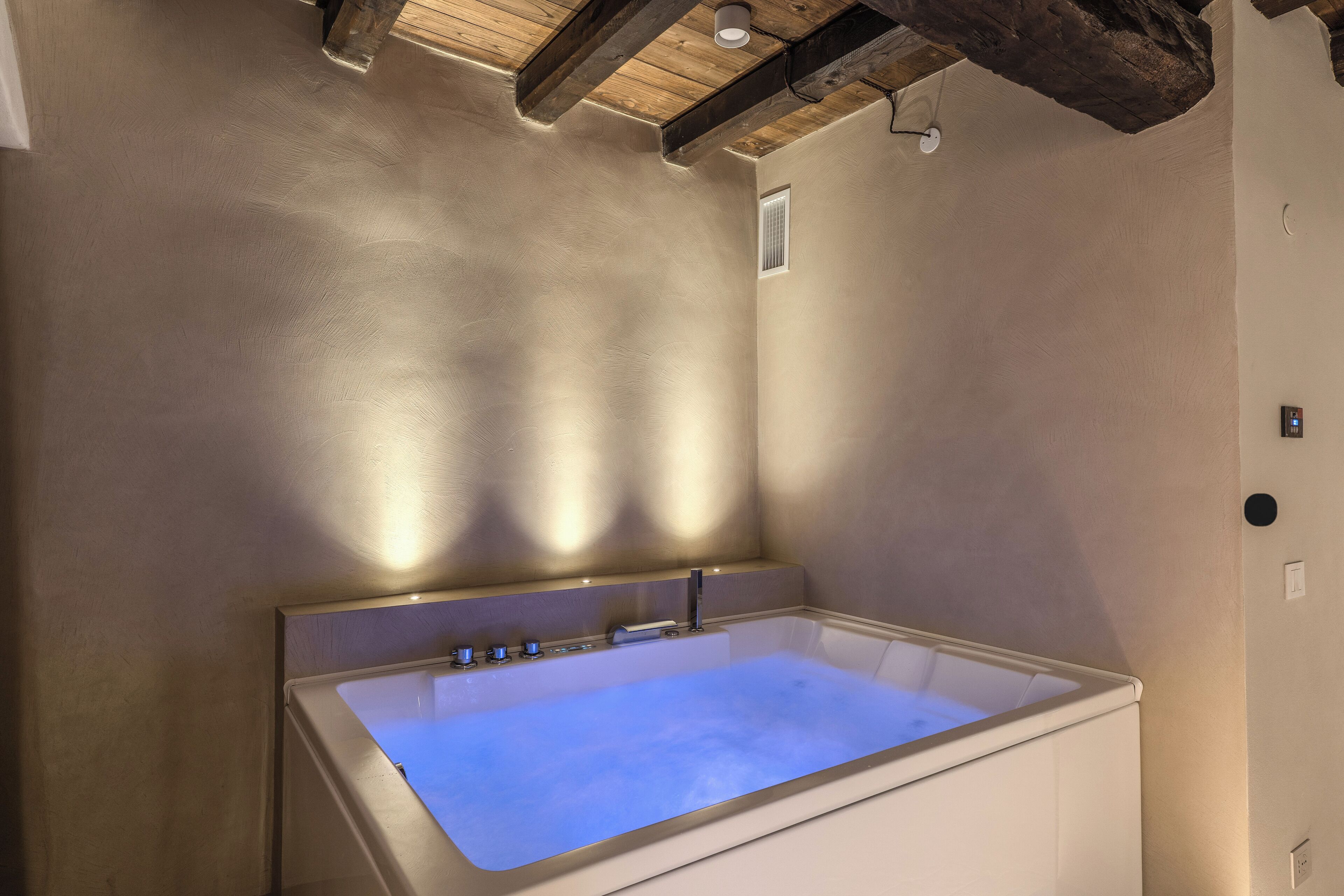 A modern bathroom with a large bathtub, wooden beams on the ceiling, and a small window.