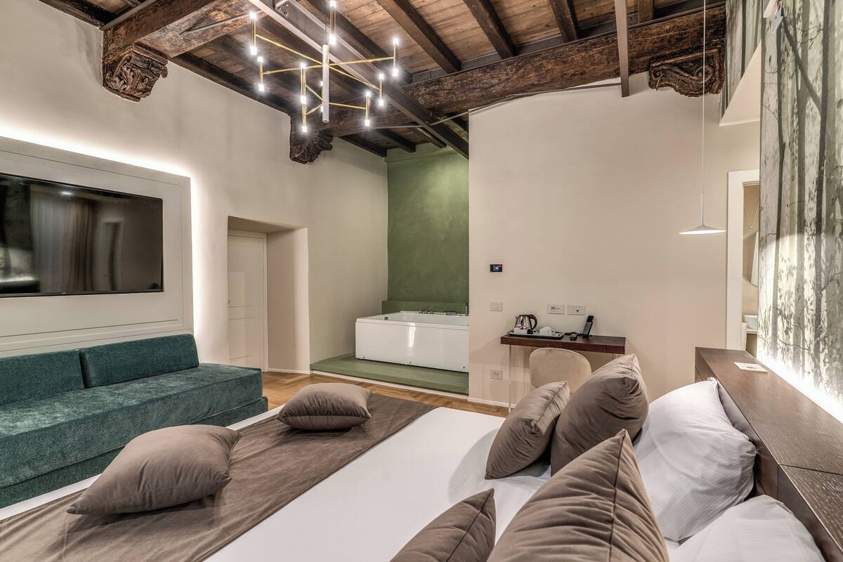 A modern bedroom with a large bed, a green sofa, a wooden ceiling, and a large window.