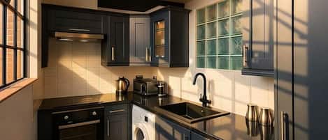 Cocina moderna con armarios oscuros, lavadora integrada, un lavamanos y un ventanal con vidrio tintado de verde.
