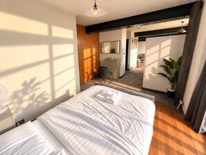 A bedroom with a large bed, a desk, a chair, and a potted plant.