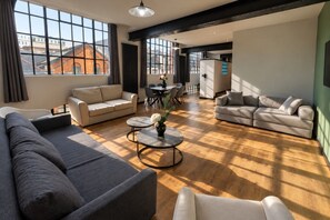 A spacious living room with a large sofa, a smaller sofa, a coffee table, and a dining area with chairs and a table.