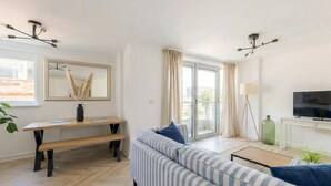 Een moderne woonkamer met een bank, een eettafel, een televisie en een groot raam met gordijnen.