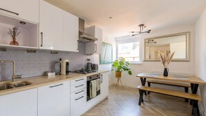 Een moderne keuken met witte kastjes, een houten aanrecht, een fornuis en een eethoek met een bank en tafel.
