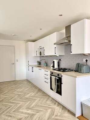 Una cocina moderna con armarios blancos, piso de madera en patrón de espiga y electrodomésticos integrados, horno y cocina a gas.
