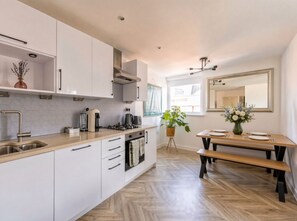 Une cuisine moderne avec des meubles blancs, un plan de travail en bois et un coin repas comprenant un banc et une table.
