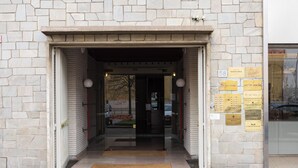 A stone building entrance with a glass door, a doormat, and plaques on the wall. - Bel Fiore 58 (Florence)