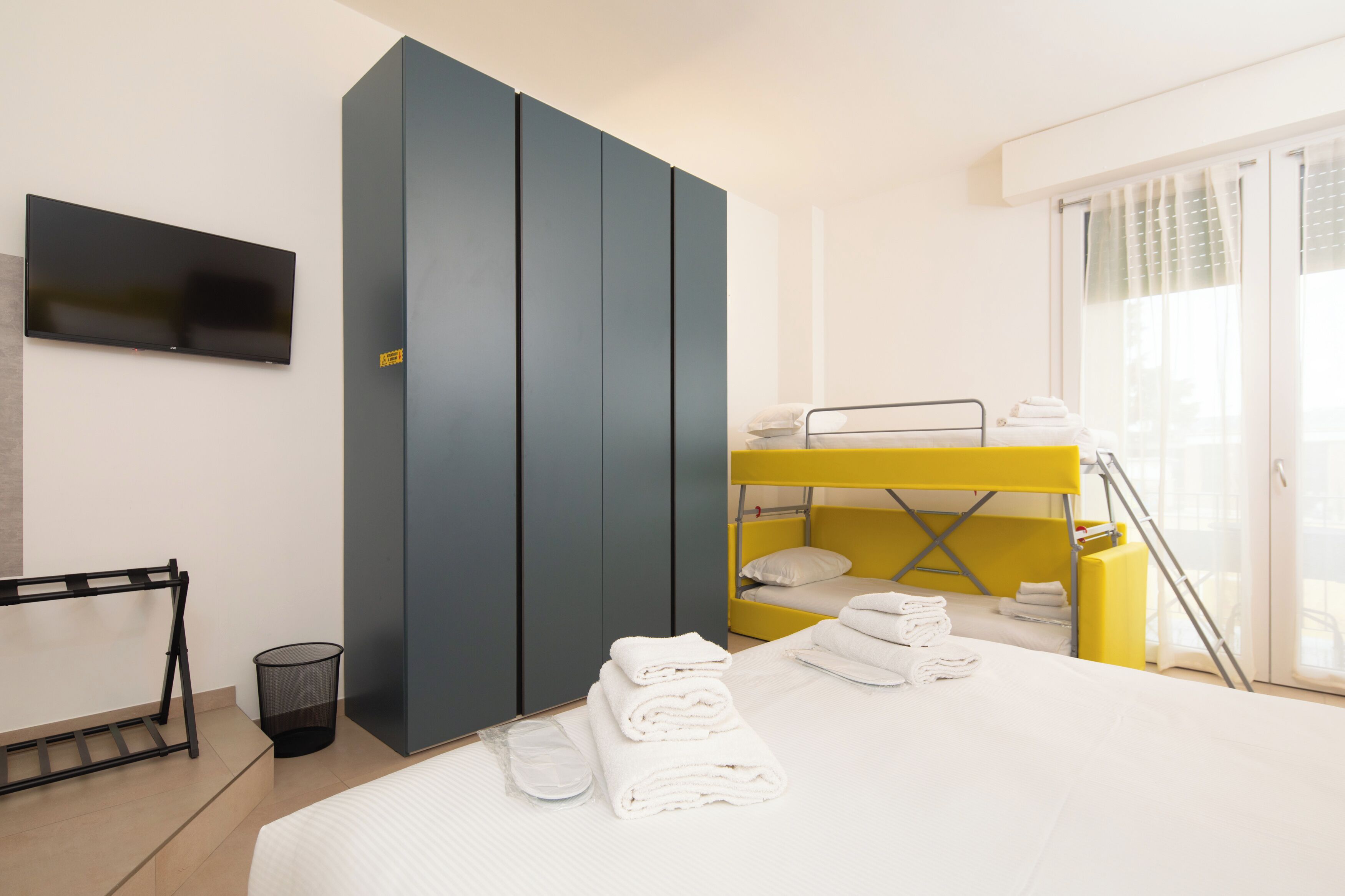 Una camera d'albergo moderna con un letto, una televisione, un armadio e un letto a castello.