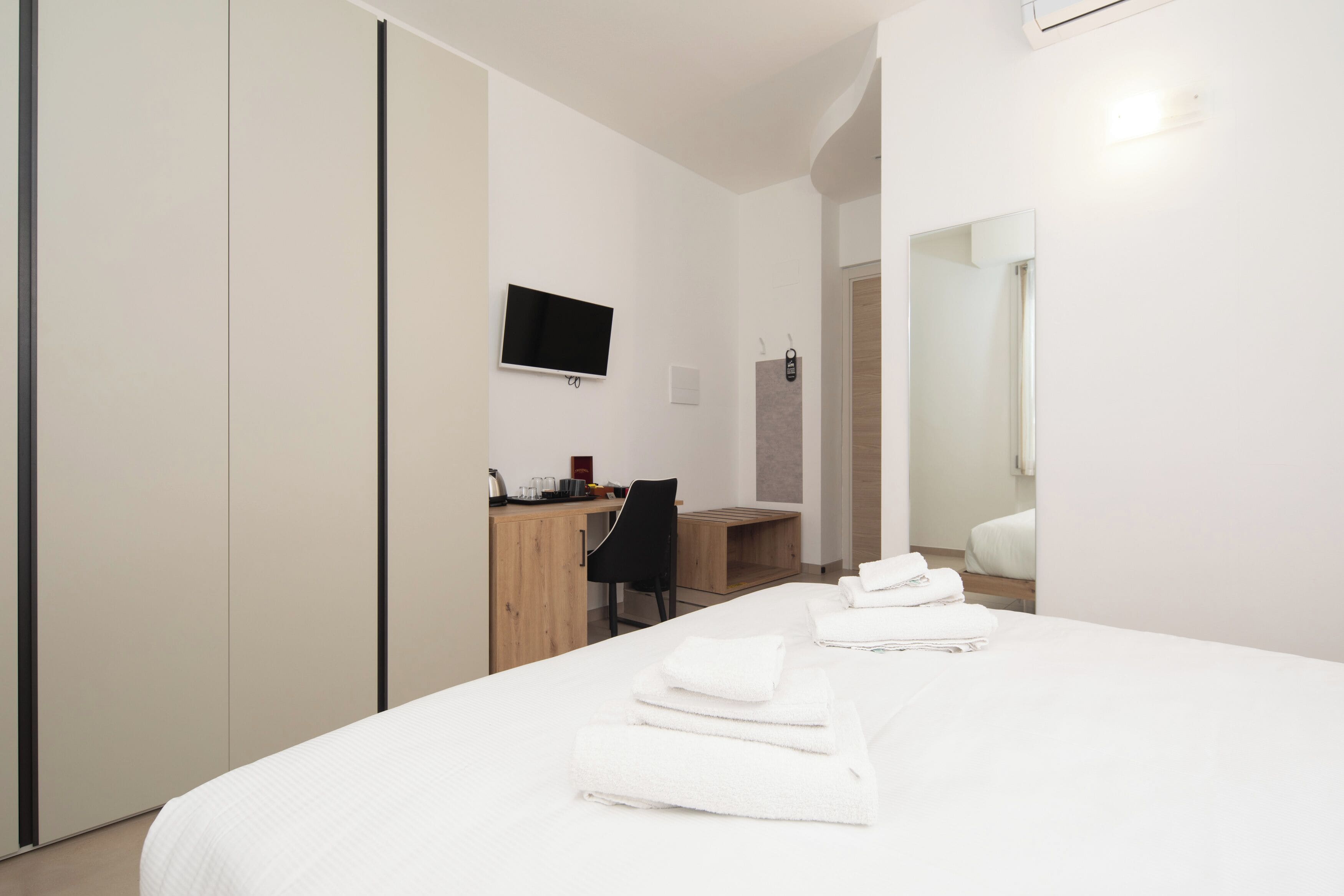 A hotel room with a bed, a desk with a chair, a TV, and a mirror.