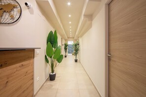 A hallway with a wooden reception desk, potted plants, a security camera, and a door at the end. - Bel Fiore 58 (Florence)