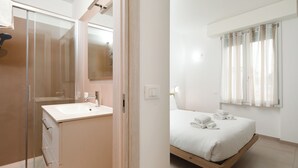 A modern hotel room with a glass shower enclosure, a white sink, a wooden bed, and a large window with curtains. - Bel Fiore 58 (Florence)
