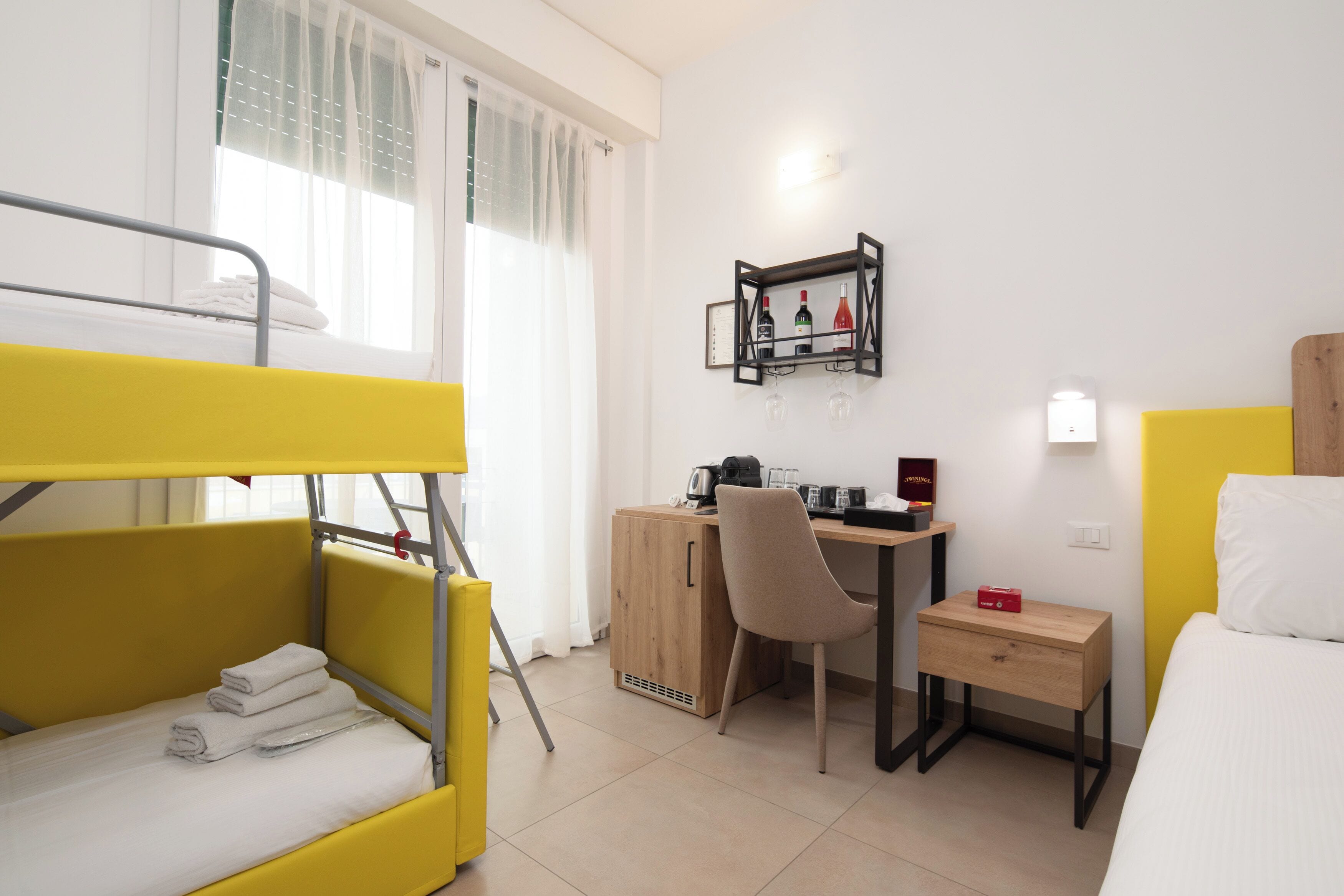 A room with a bunk bed, a desk with a chair, a small bedside table, and a bed.