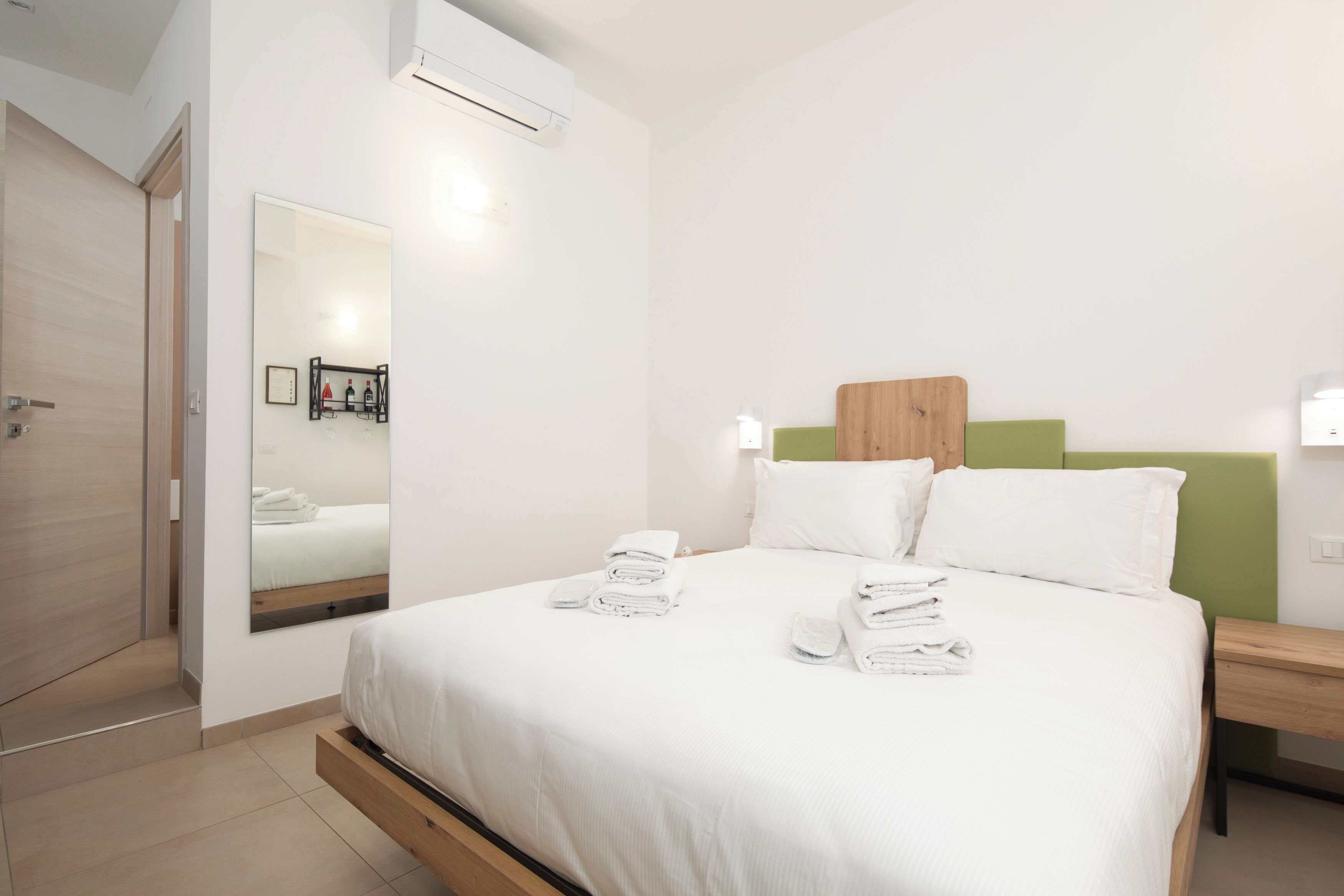 Habitació d'hotel moderna amb llit, taules de nit, un mirall i un capçal de llit verd.