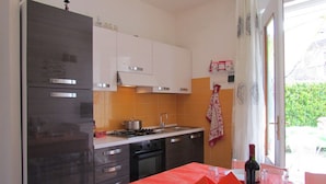 Une cuisine équipée d’un réfrigérateur, d’une cuisinière et d’un évier. On y trouve une table mise pour le repas, avec des assiettes, des verres et une bouteille.
