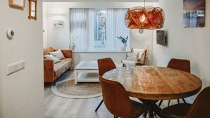 Ett modernt vardagsrum med ett runt matbord i trä, en brun lädersoffa och ett stort fönster med tunna, genomskinliga gardiner.
