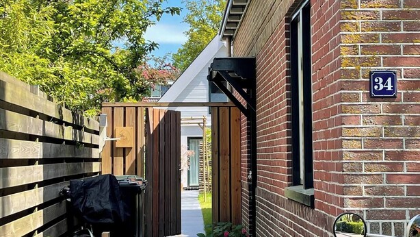 En smal gång leder fram till en byggnad av tegel med skylten nummer 34, och den är omgiven av trästaket och växter.