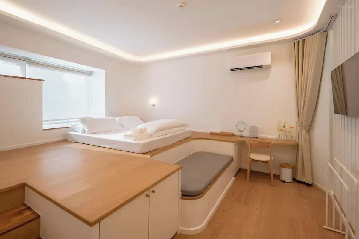 A compact, modern room with a bed, a desk, and a bench.