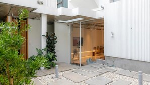 A modern building with a glass entrance, outdoor seating, and a garden area with plants and stepping stones. - Vaeh Viean Silom (Bangkok)