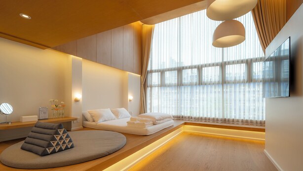 A modern hotel room with a wooden floor, a sofa bed, a bedside table with a lamp, and a large window with sheer curtains. - Vaeh Viean Silom (Bangkok)
