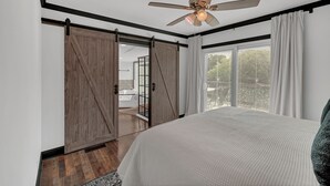 Un dormitorio con una cama grande, ventilador de techo, puertas correderas estilo granero y vistas al exterior.