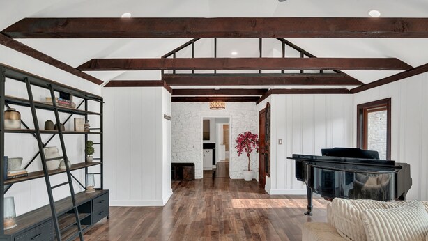 Amplia habitación con suelo de madera, un piano negro y una pared de piedra blanca.