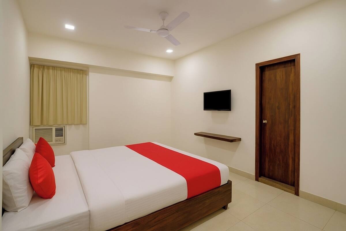 A bedroom with a bed, a ceiling fan, a TV, a wooden door, and a window with curtains.