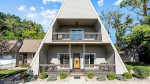 A two-story house with a central balcony, a front door, and a small porch with railings. - A-Frame Home | Ultimate Retreat in Bourbon Country (Coxs Creek)