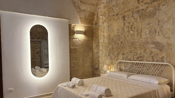 Ein Schlafzimmer mit Steinsandsteinwand, einem großen Spiegel, einem Bett mit weißen Leinen und einem kleinen Tisch mit Lampe.
