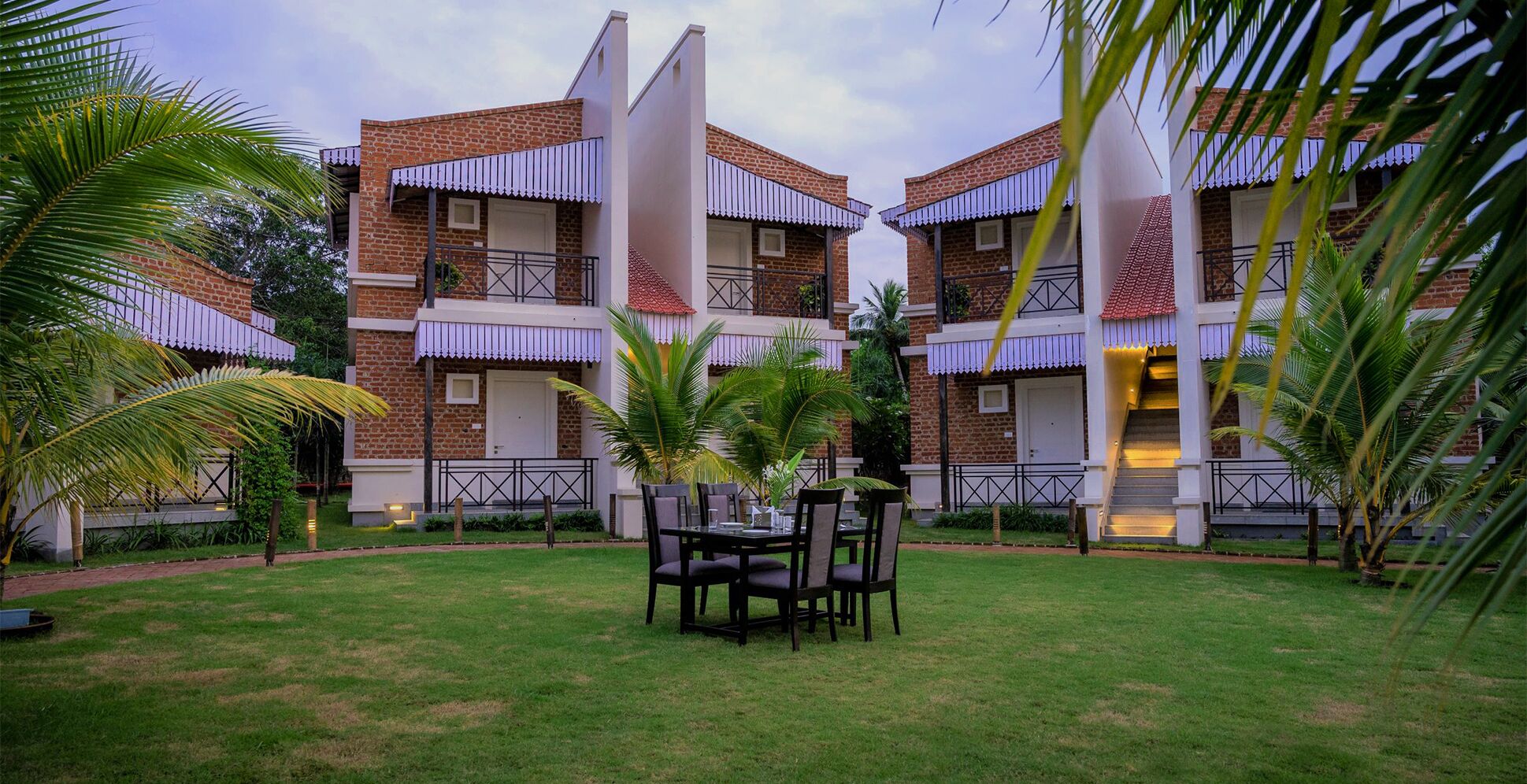 A courtyard with a dining table and chairs, surrounded by brick buildings with balconies and a palm tree.