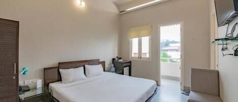 A hotel room with a bed, a desk, a chair, a TV on the wall, and a balcony with a view.