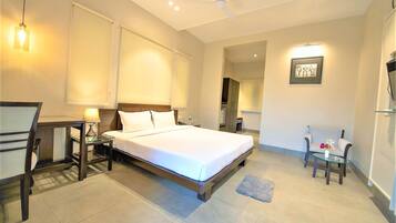 A hotel room with a bed, bedside tables, a desk, a chair, and a small table with a vase.