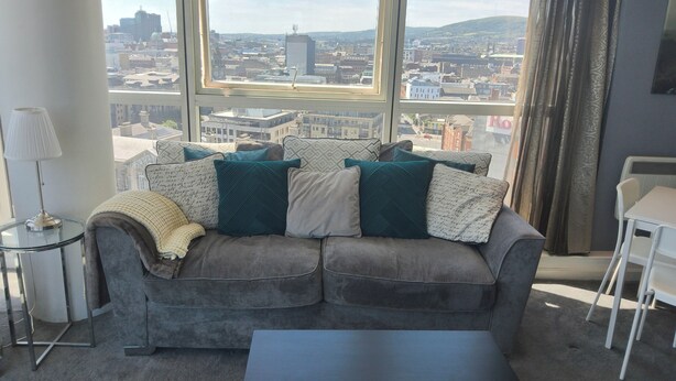 A living room with a grey sofa, a black coffee table, and a view of a cityscape through large windows. - City Centre high rise (Belfast)
