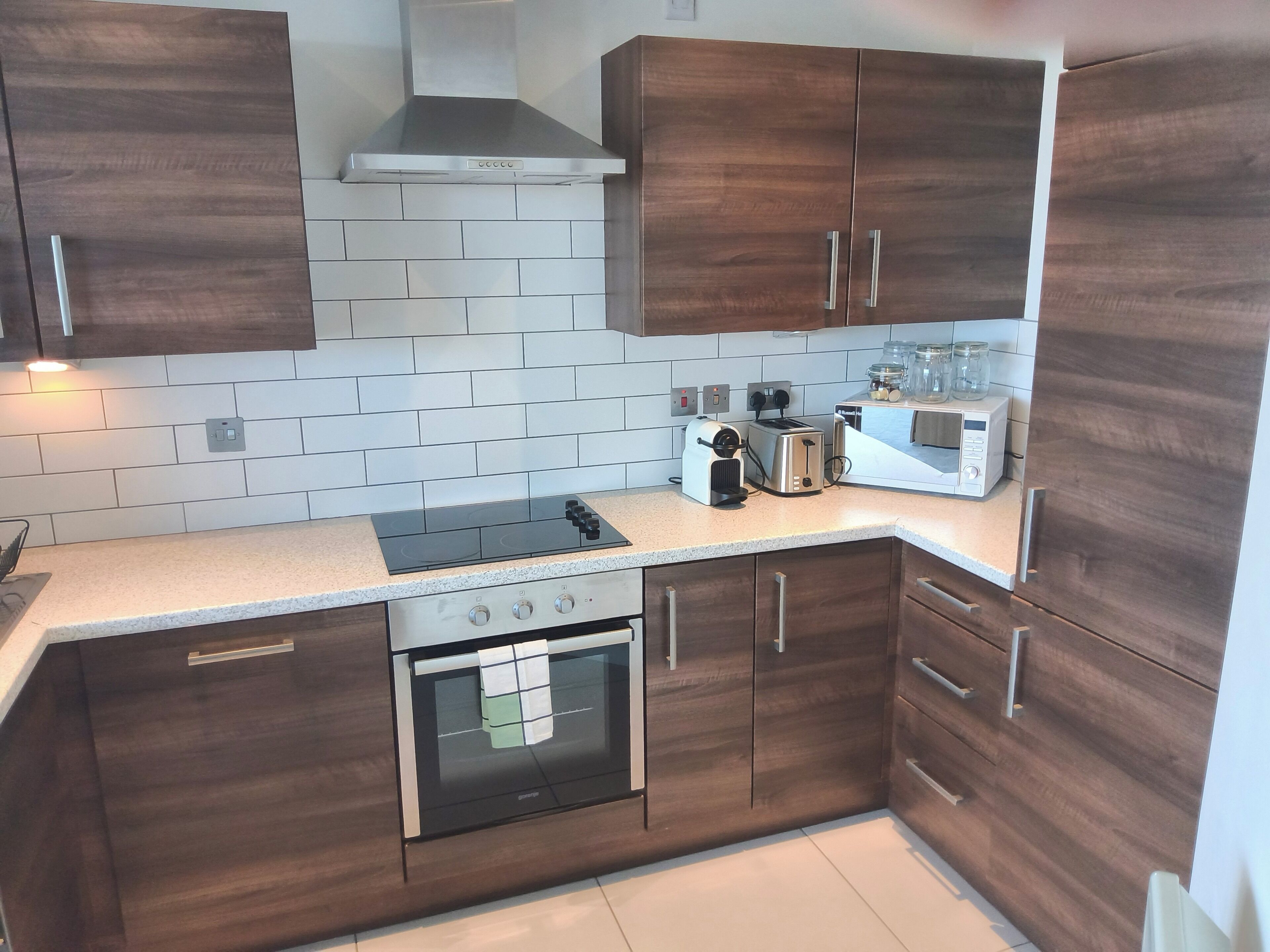 A modern kitchen with dark wooden cabinets, a stainless steel range hood, a built-in oven, a gas stove, a toaster, and a coffee maker.