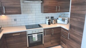 A modern kitchen with dark wooden cabinets, a stainless steel range hood, a built-in oven, a gas stove, a toaster, and a coffee maker. - City Centre high rise (Belfast)