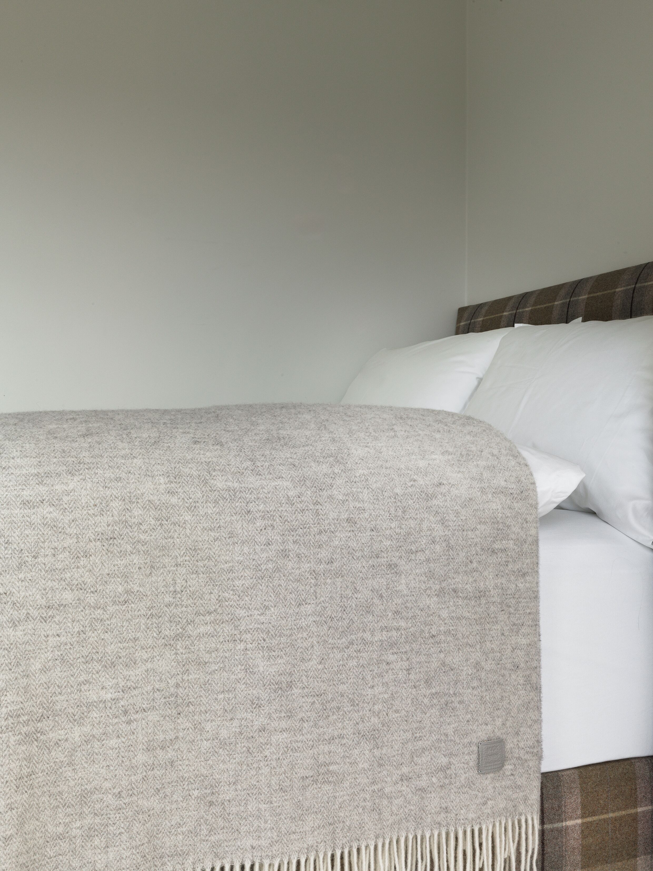 A bed with a grey blanket and white pillows.