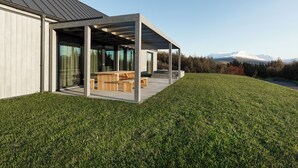 Una casa moderna con un porche cubierto, césped y vistas a la montaña.