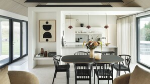 Un comedor moderno con una mesa y sillas negras, un florero con flores y vistas a la cocina a través de una puerta abierta.